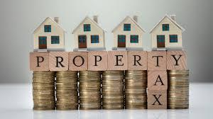 small homes on top of scrabble blocks on top of coins. The blocks spell "Property Tax"