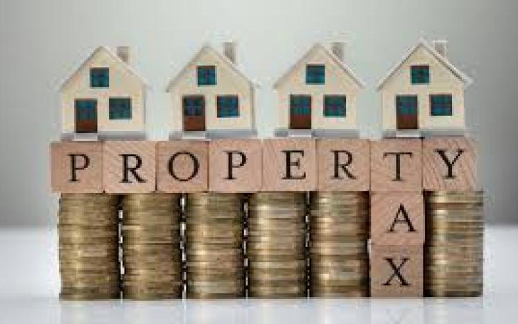 small homes on top of scrabble blocks on top of coins. The blocks spell "Property Tax"